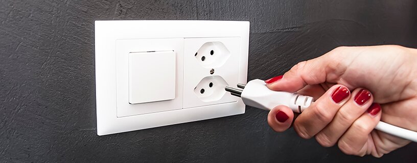 Wand mit Schweizer Steckdose; weibliche Hand hält Stromkabel in der Hand